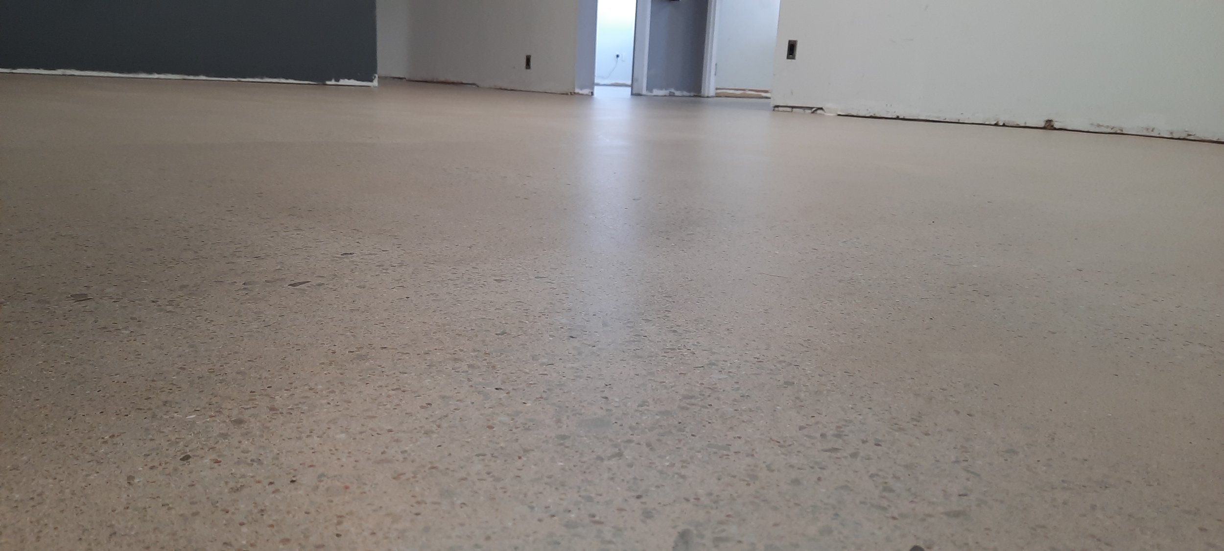 Interior of a room under construction with a beige floor, unfinished walls, and doorways leading to other rooms.