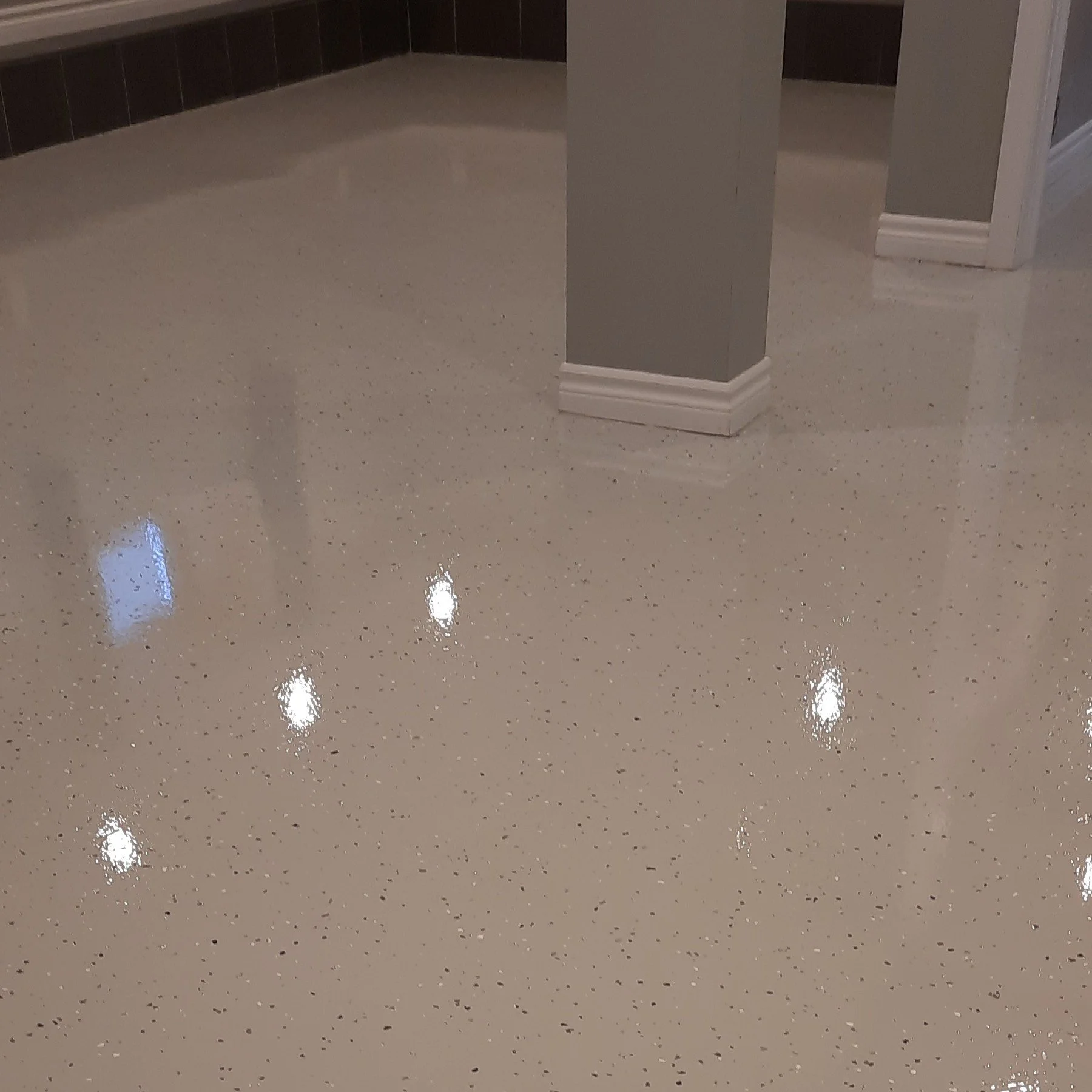 Polished beige terrazzo flooring with small dark and light flecks, reflecting overhead lights.