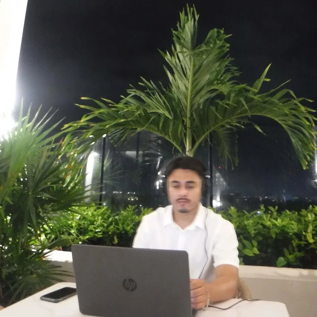 Aarón Tapia trabajando en una laptop en un entorno con plantas tropicales y un fondo oscuro