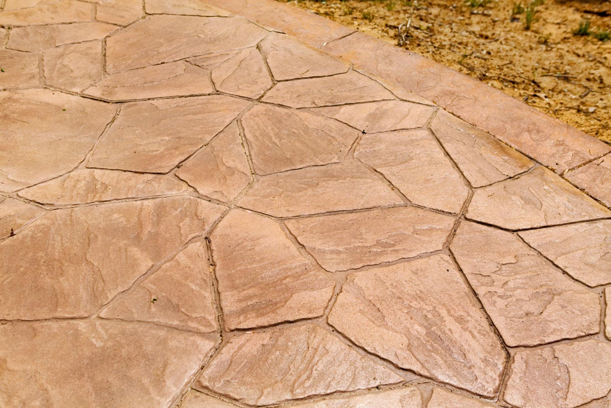 Close-up of a patterned stone walkway with irregular pinkish stones and sand in the background.