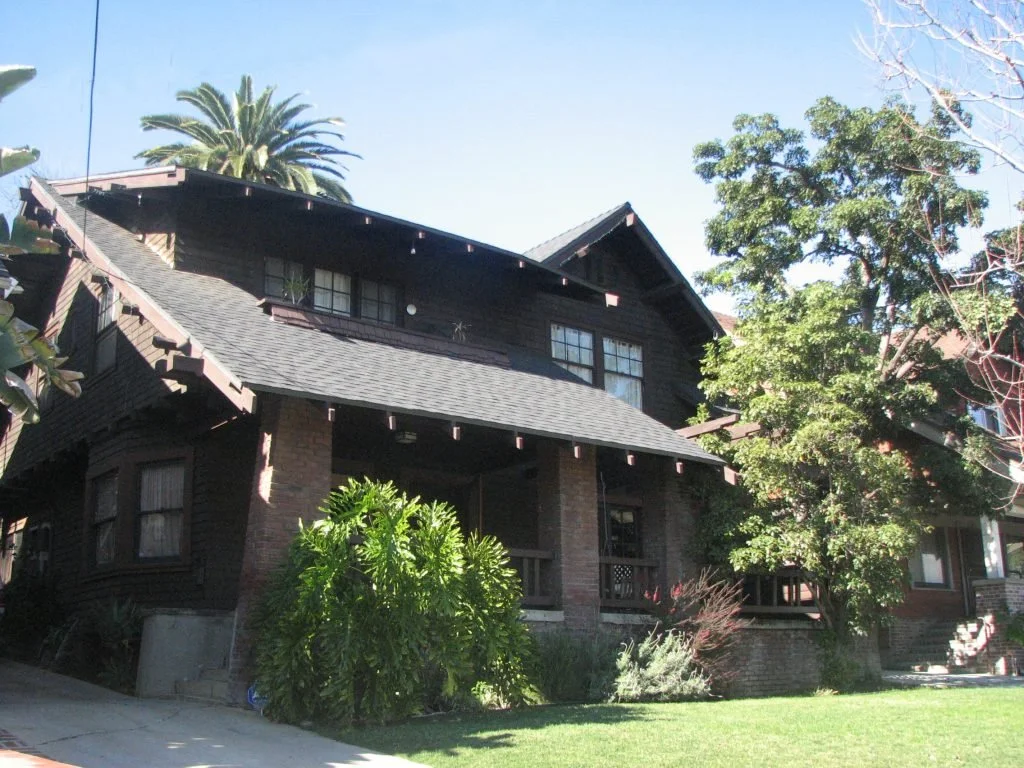 This stately Craftsman at 534 N Avenue 54 is dominated by a handsome concrete porch with two battered brick columns on either end. Above the left side of the porch is a sheltered balcony and a gable on the right side is located above an arbor. The ea