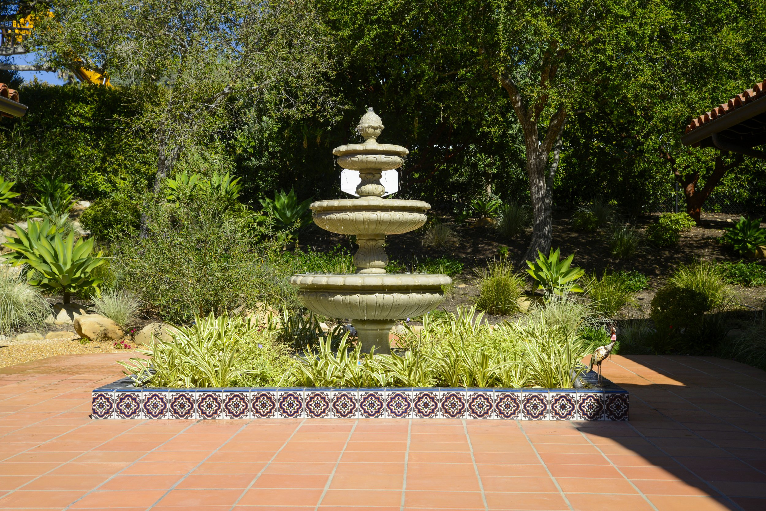A multi-tiered stone fountain surrounded by plants and decorative tiles in a garden.
