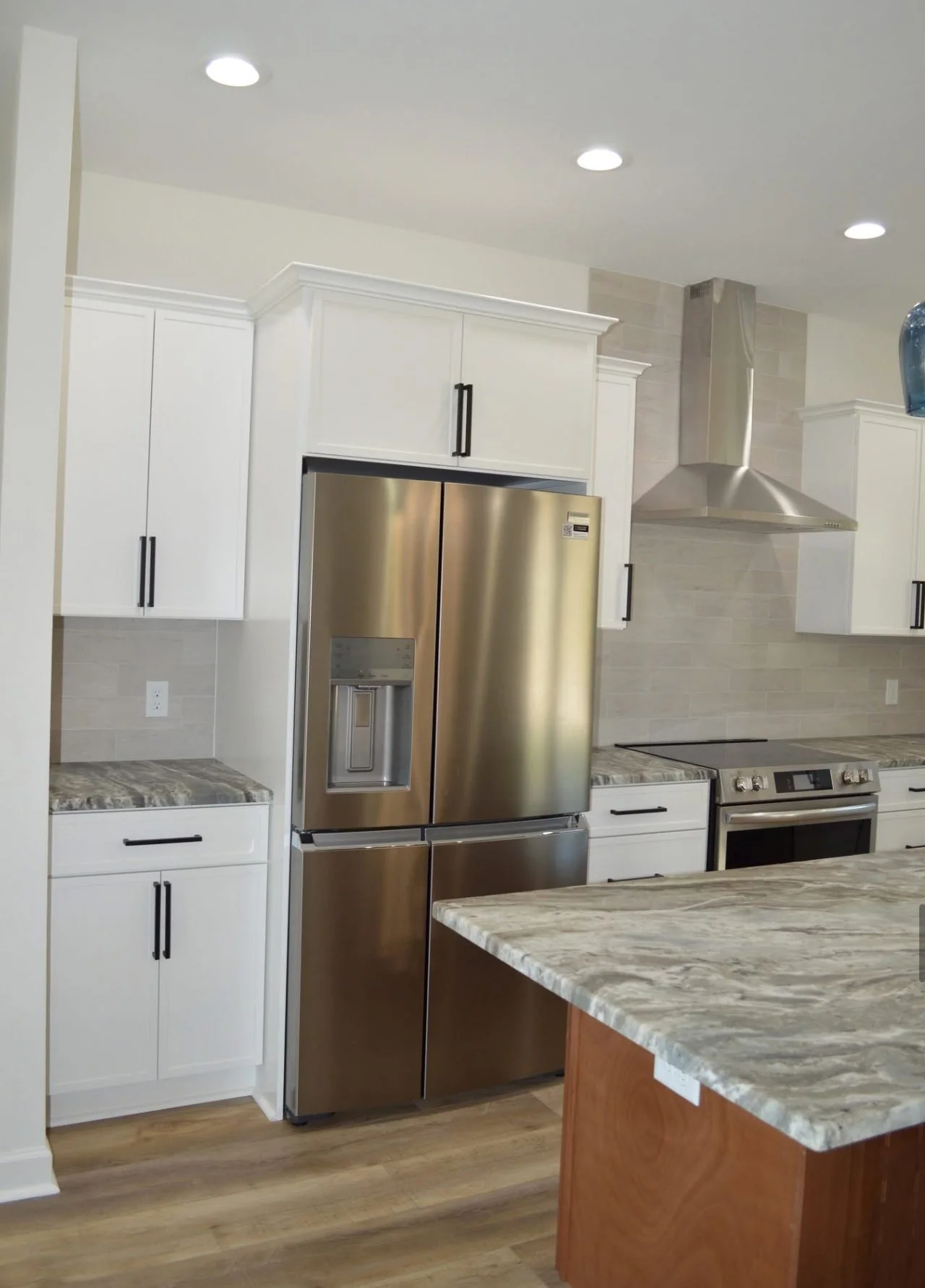 Modern kitchen with white cabinets, stainless steel refrigerator, marble countertop island, and stainless steel stove with vent hood.