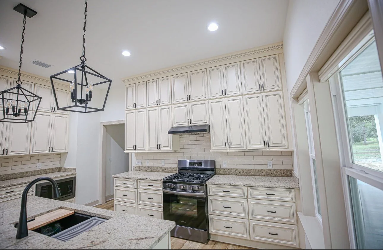 Kitchen with cream-colored cabinets, granite countertops, a black stove, microwave, and two pendant lights with geometric black frames.