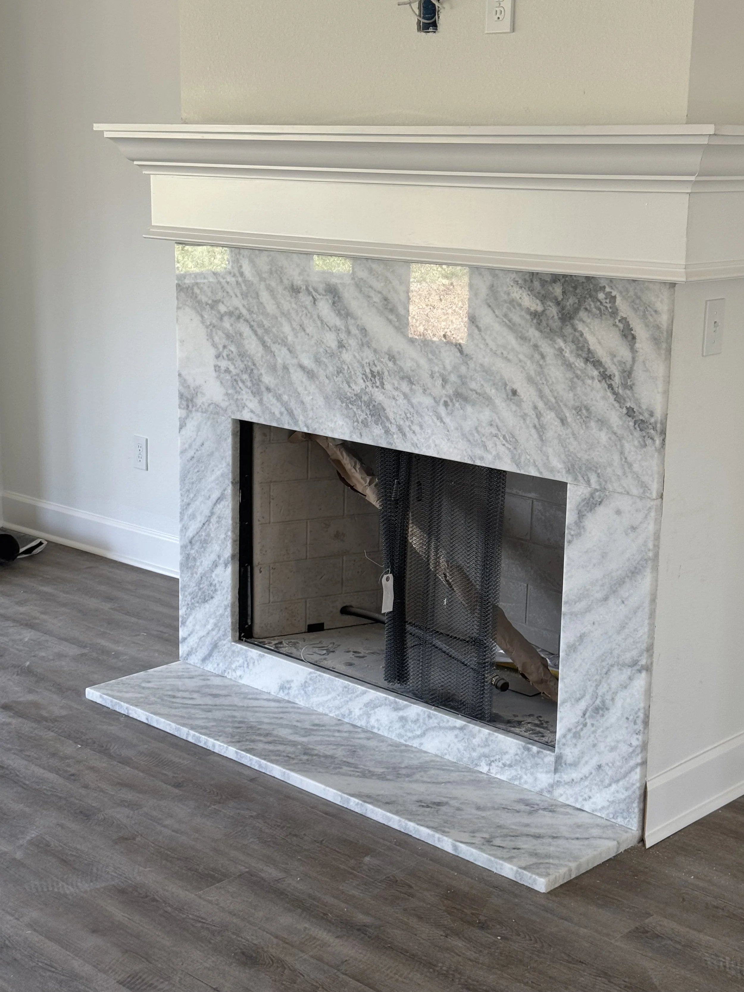 White marble fireplace with gray veining, white mantel, and hearth, with construction materials inside the firebox.