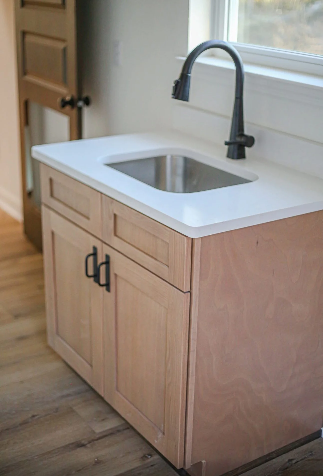 Small kitchen sink with a black faucet, installed in a wooden cabinet under a window, in a cozy kitchen.