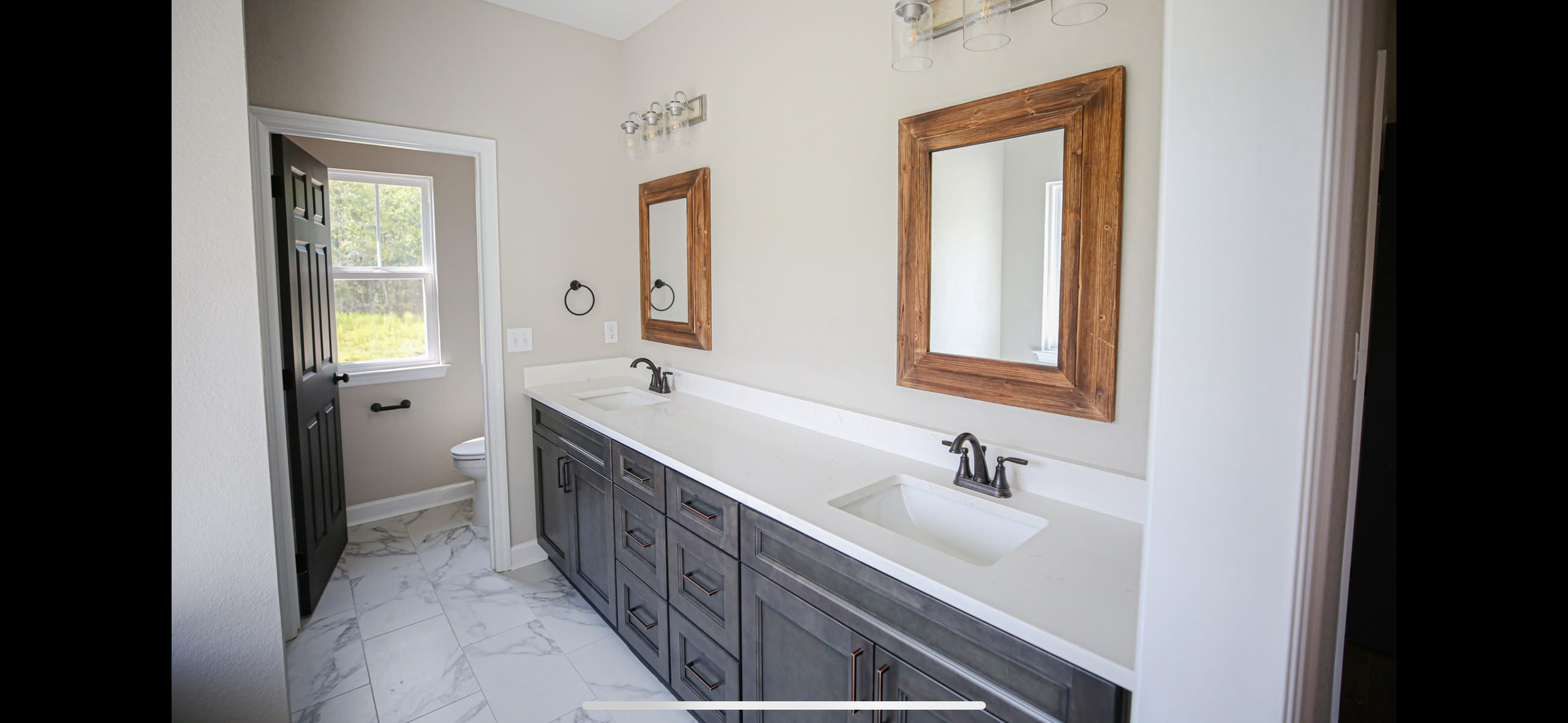 Bathroom with dual sinks, dark wood cabinets, two mirrors with wooden frames, and a window in the toilet area.