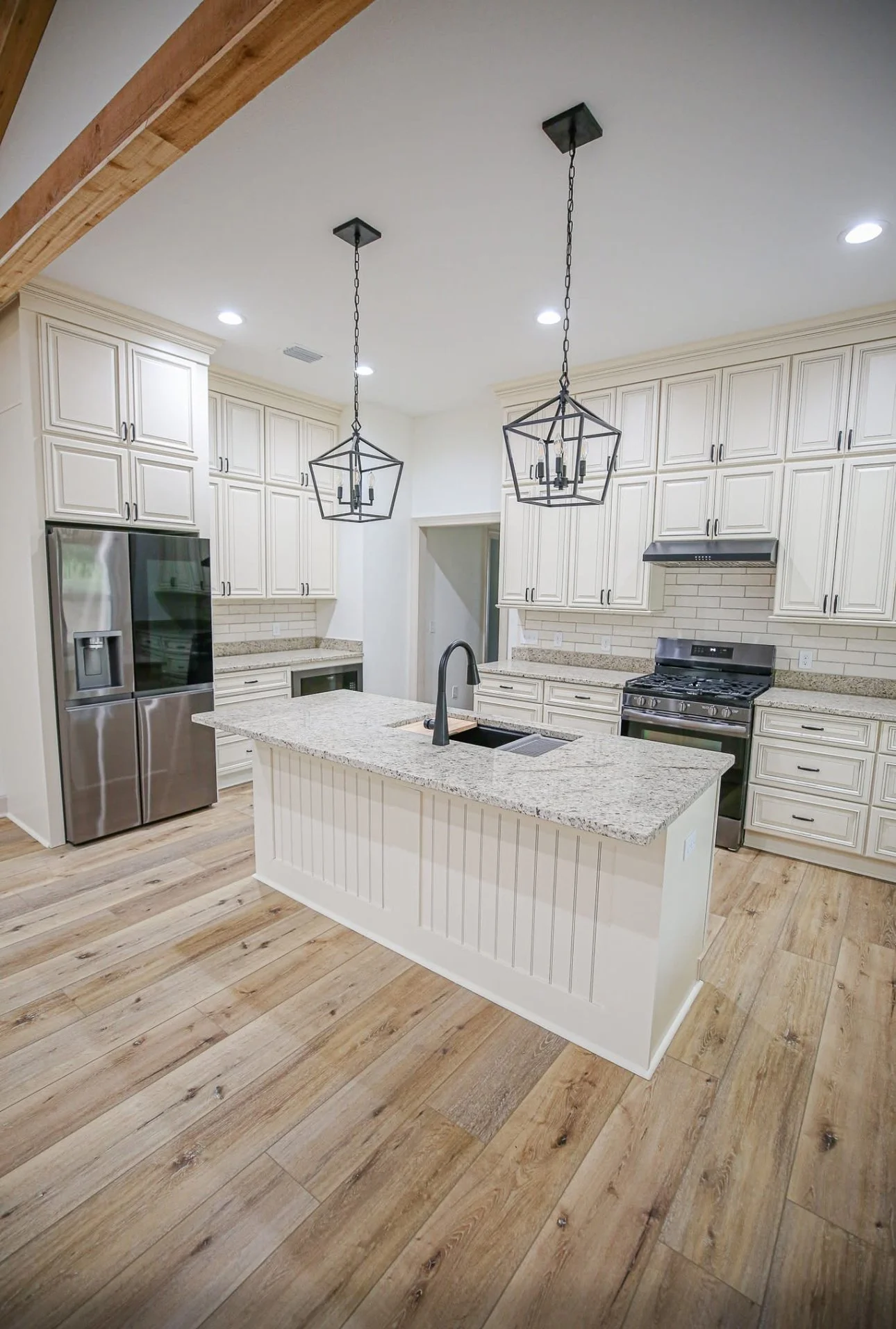 A modern kitchen with white cabinets, a granite island, stainless steel appliances, and wood flooring.