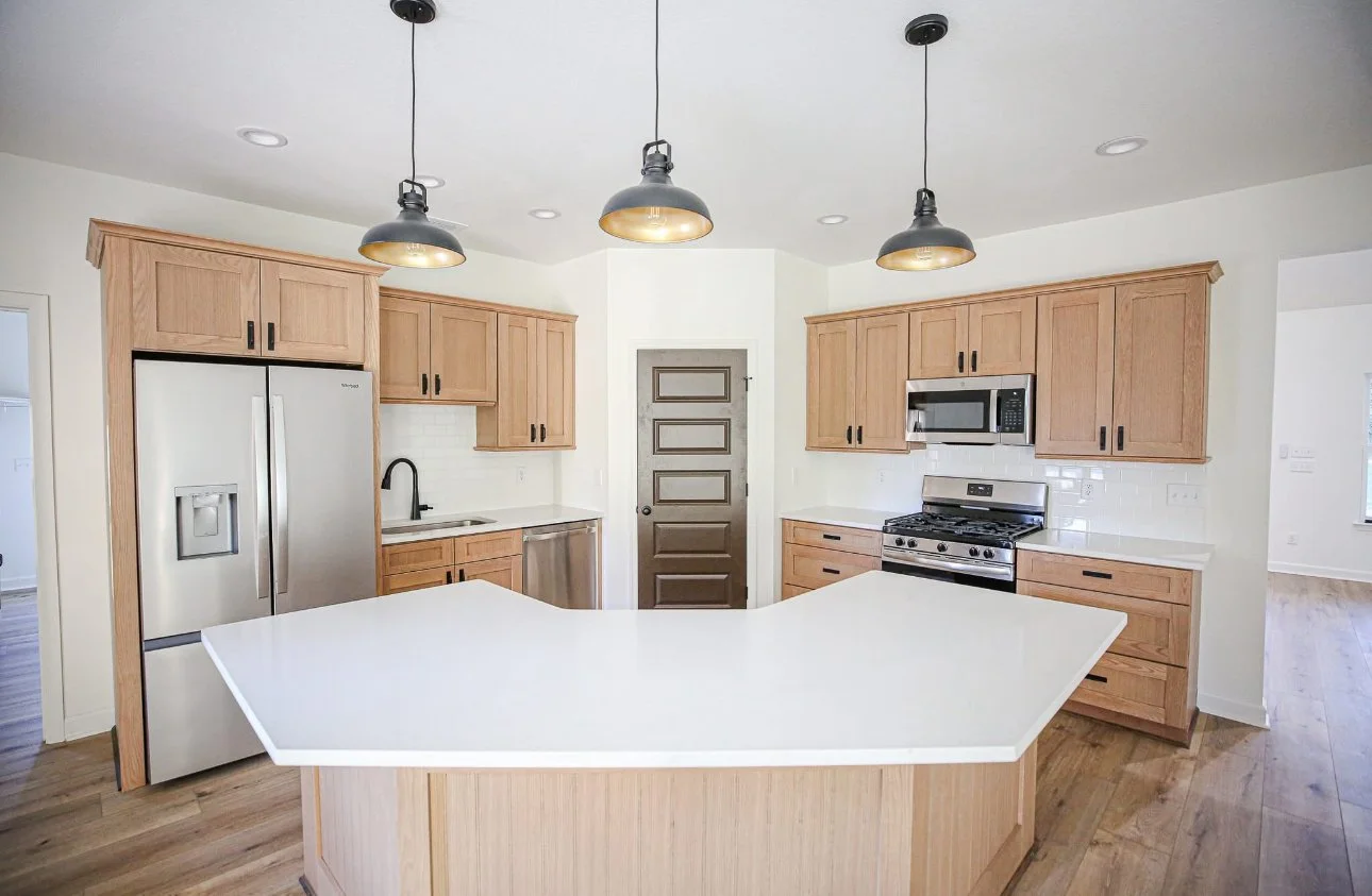 Kitchen with wooden cabinets, a stainless steel refrigerator, a gas stove with an over microwave, a centered island with a white countertop, and pendant lighting.