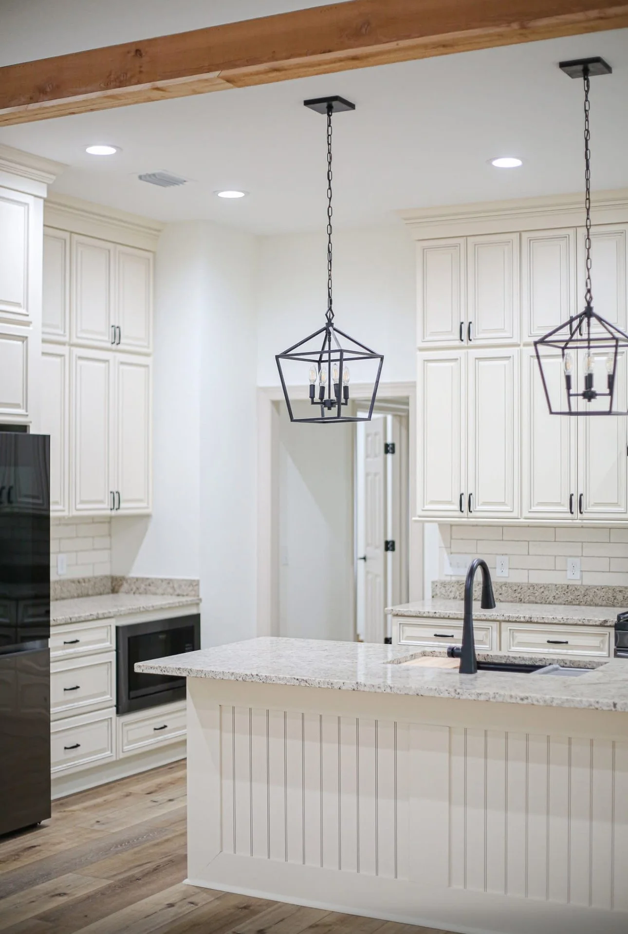 Modern kitchen with white cabinets, granite countertops, black hardware, and two black geometric hanging pendant lights.