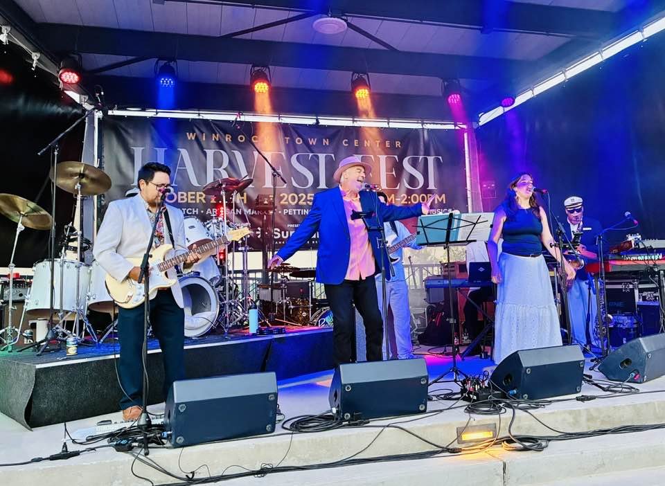 Henry Sutro performing Yacht Rock at Winrock outdoor concert in Albuquerque, NM, a guitarist, a keyboardist, and a drummer. The stage is decorated with colorful lights, and a banner in the background reads "Harv Fest October 2023."