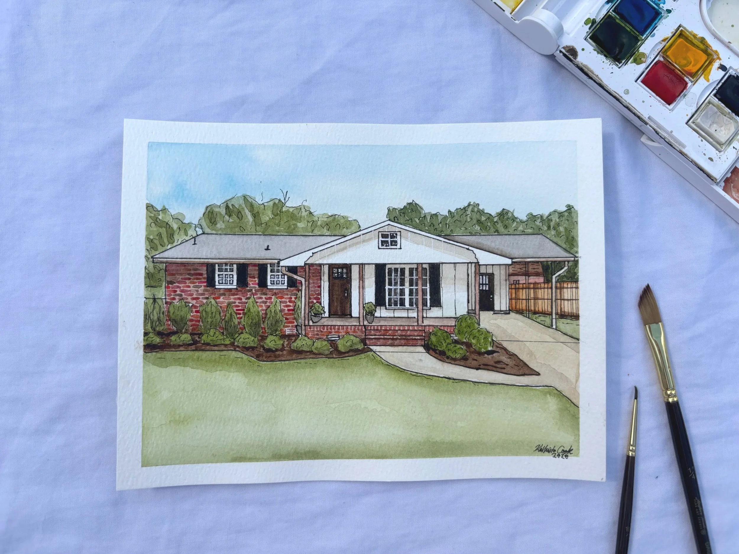 Watercolor painting of a house with a brick and white exterior, front porch, and landscaped yard with shrubs and a walkway.