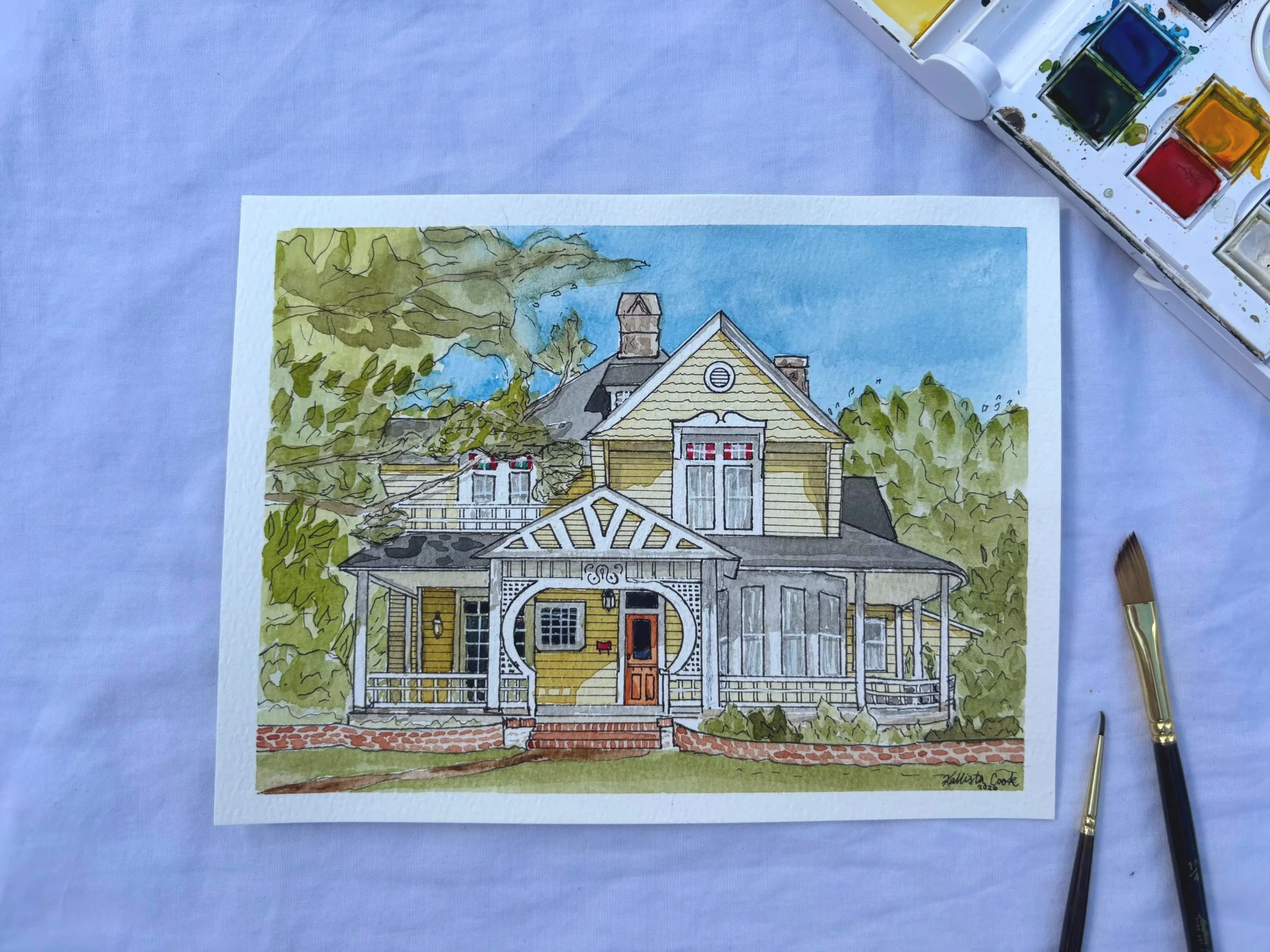 A watercolor painting of a yellow, two-story house with a detailed porch and large windows. The house has a gabled roof, a chimney, and trees surrounding it. The scene includes a blue sky with some clouds.