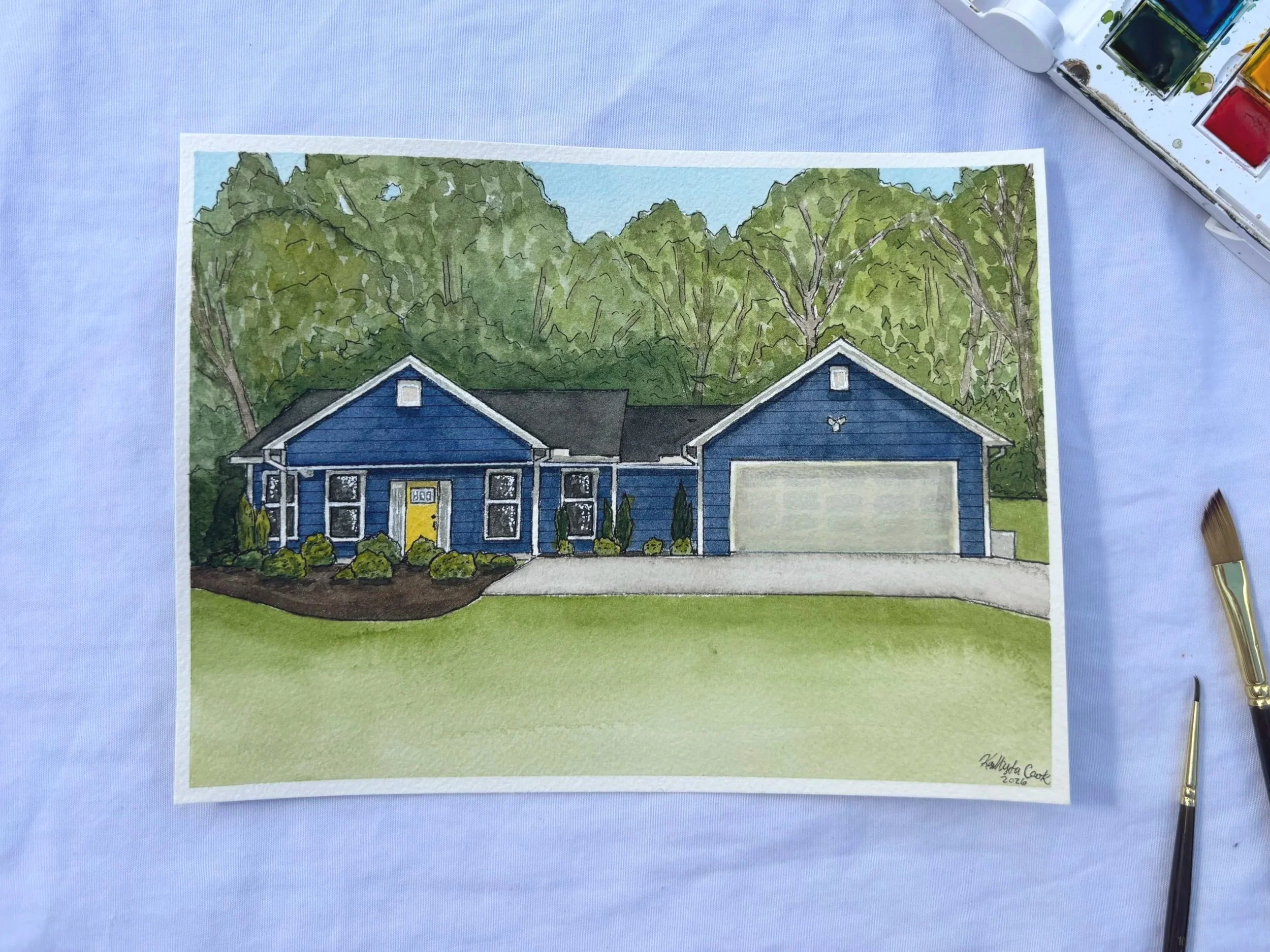 Watercolor painting of a blue house with a front yard, bushes, and trees in the background.