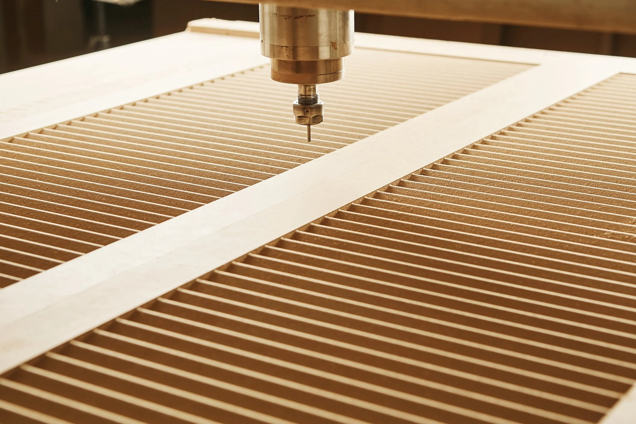 A CNC machine drill pressing down on a carved wooden surface with parallel grooves.