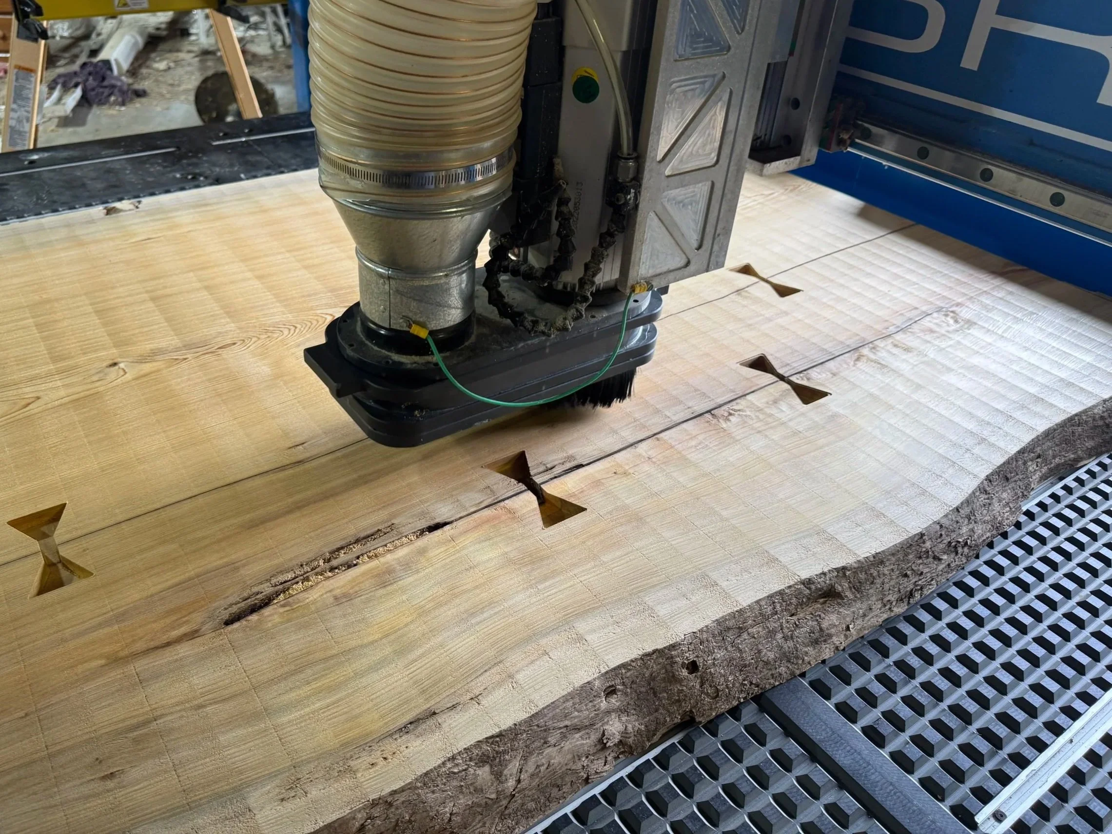 Close-up of a CNC machine carving a large piece of wood, with visible machinery and sawdust scattered around.