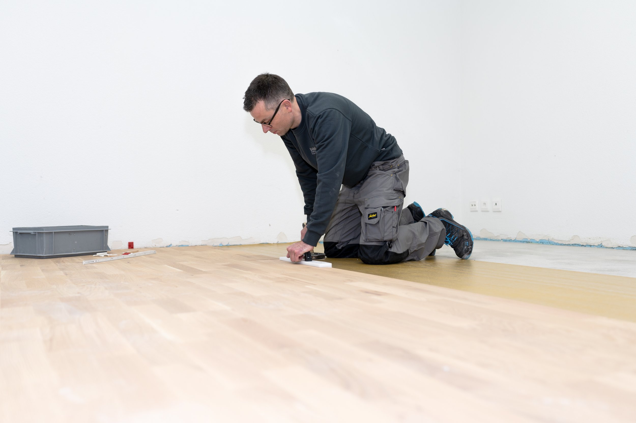 Ein Handwerker verlegt einen Holzboden im Raum.