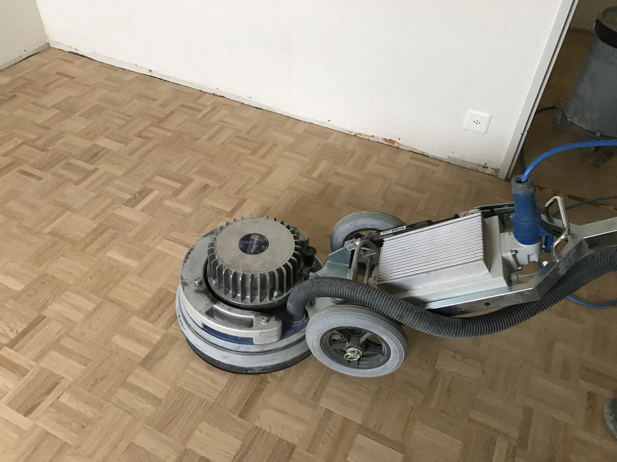 Bodenbelagsabschleifer auf Parkettboden in einem Raum.