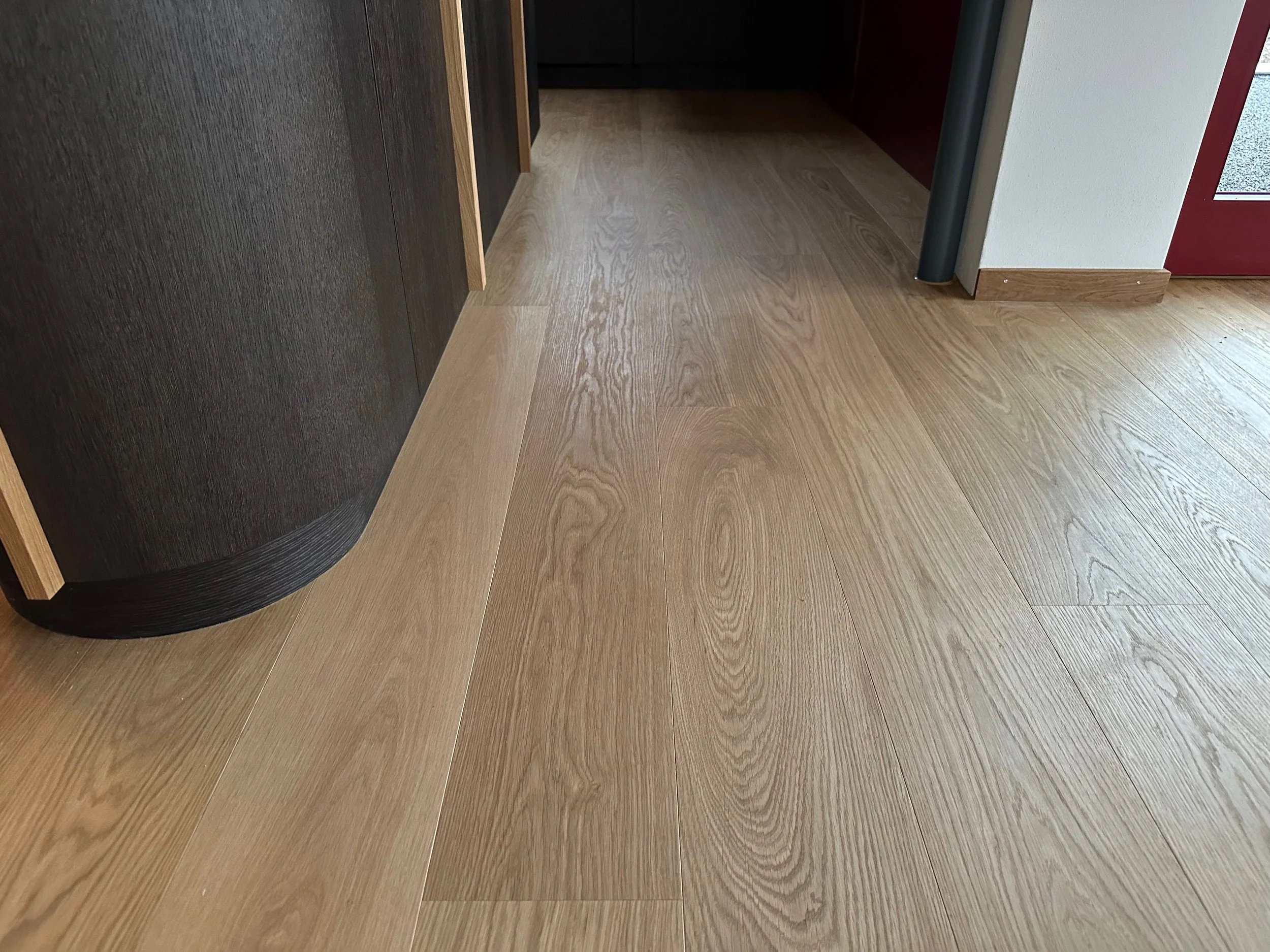 Holzfußboden in einem Raum mit Tür und Möbel, Blick auf den Boden, Holzmaserung sichtbar.