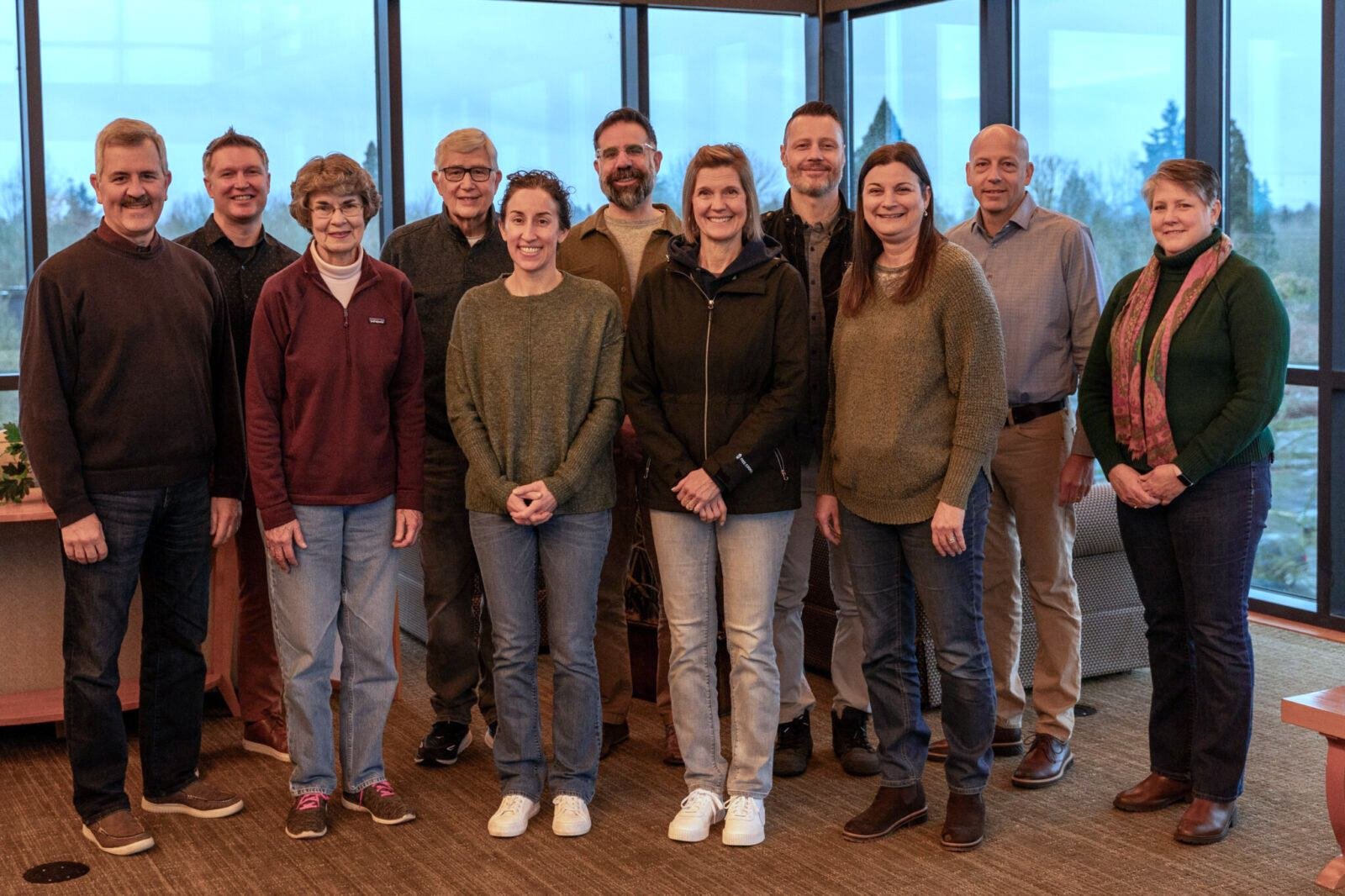 Group of eleven people standing in a room with large windows, posing for a photo.