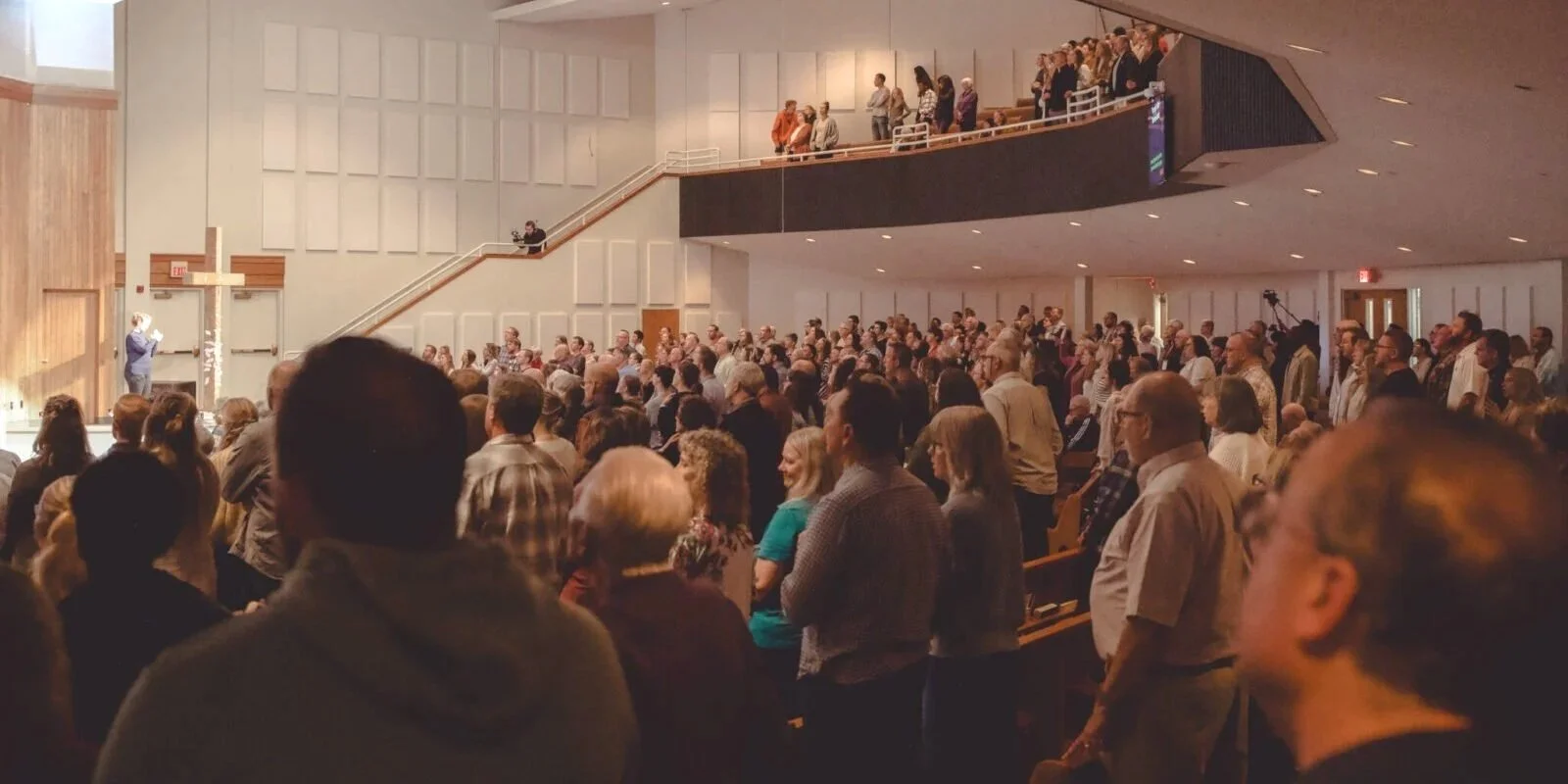 A large crowd gathered in a church for a worship service, with a cross on the wall and a speaker at the podium.