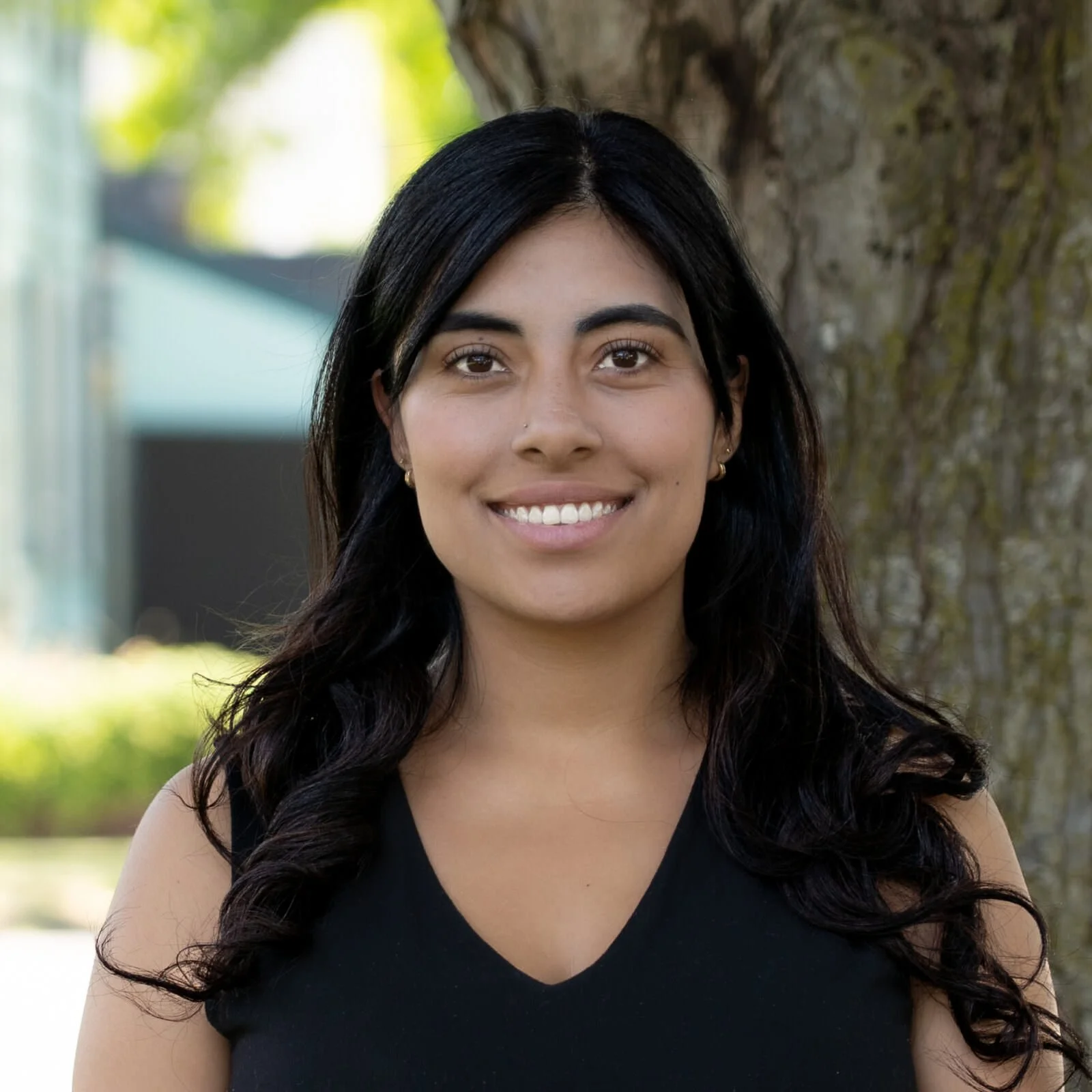 Young woman with long black hair smiling outdoors near a tree