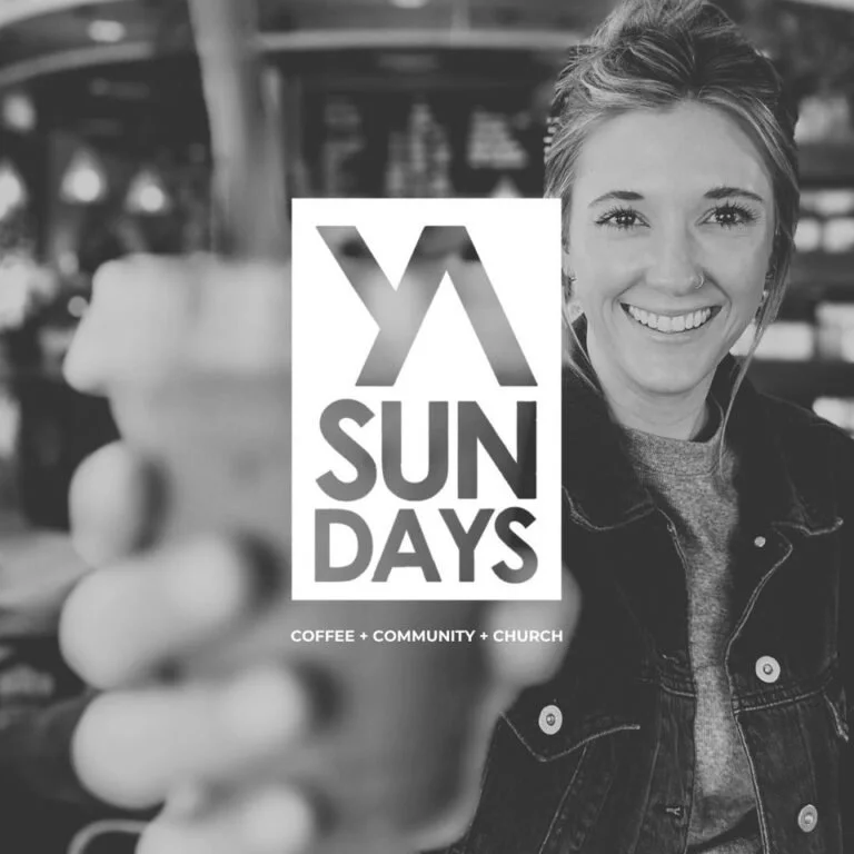 A woman smiling and holding a coffee in a coffee shop with a sign for 'Sundays' promoting coffee, community, and church.