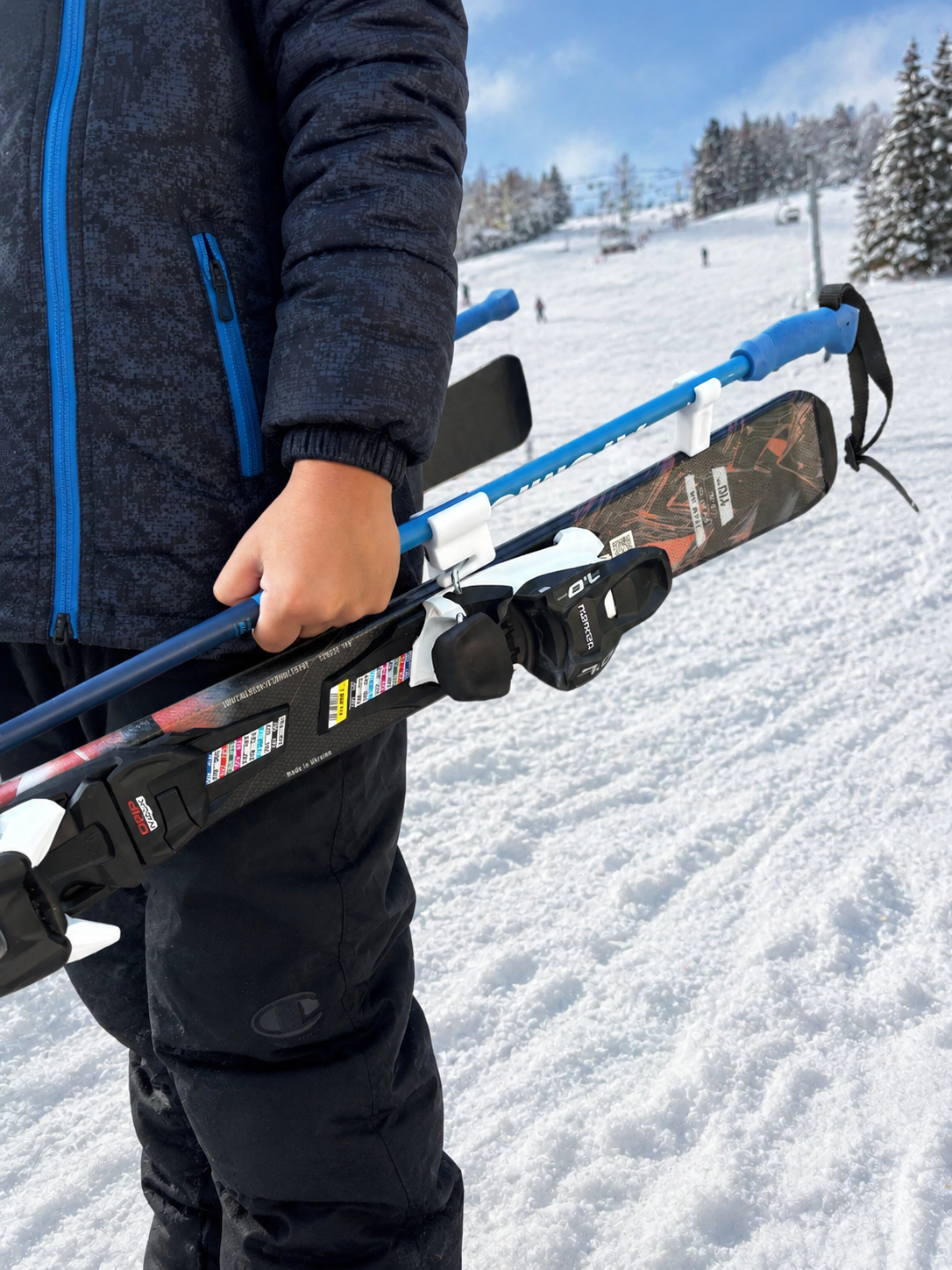 A person holding a snowboard and ski poles on a snowy mountain slope with ski lifts and other skiers in the background.