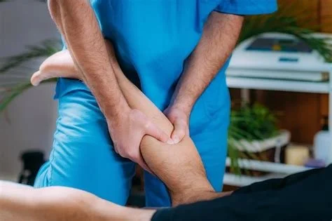 A physiotherapist performs a knee examination on a patient in a clinical setting, massaging their calf muscles.