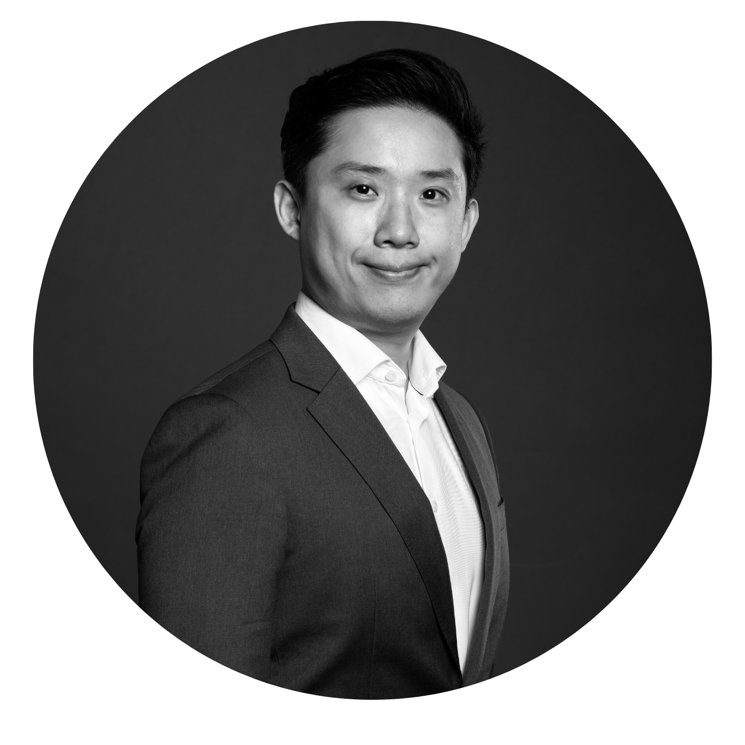 Black and white professional portrait of a young Asian man in a suit, smiling softly.
