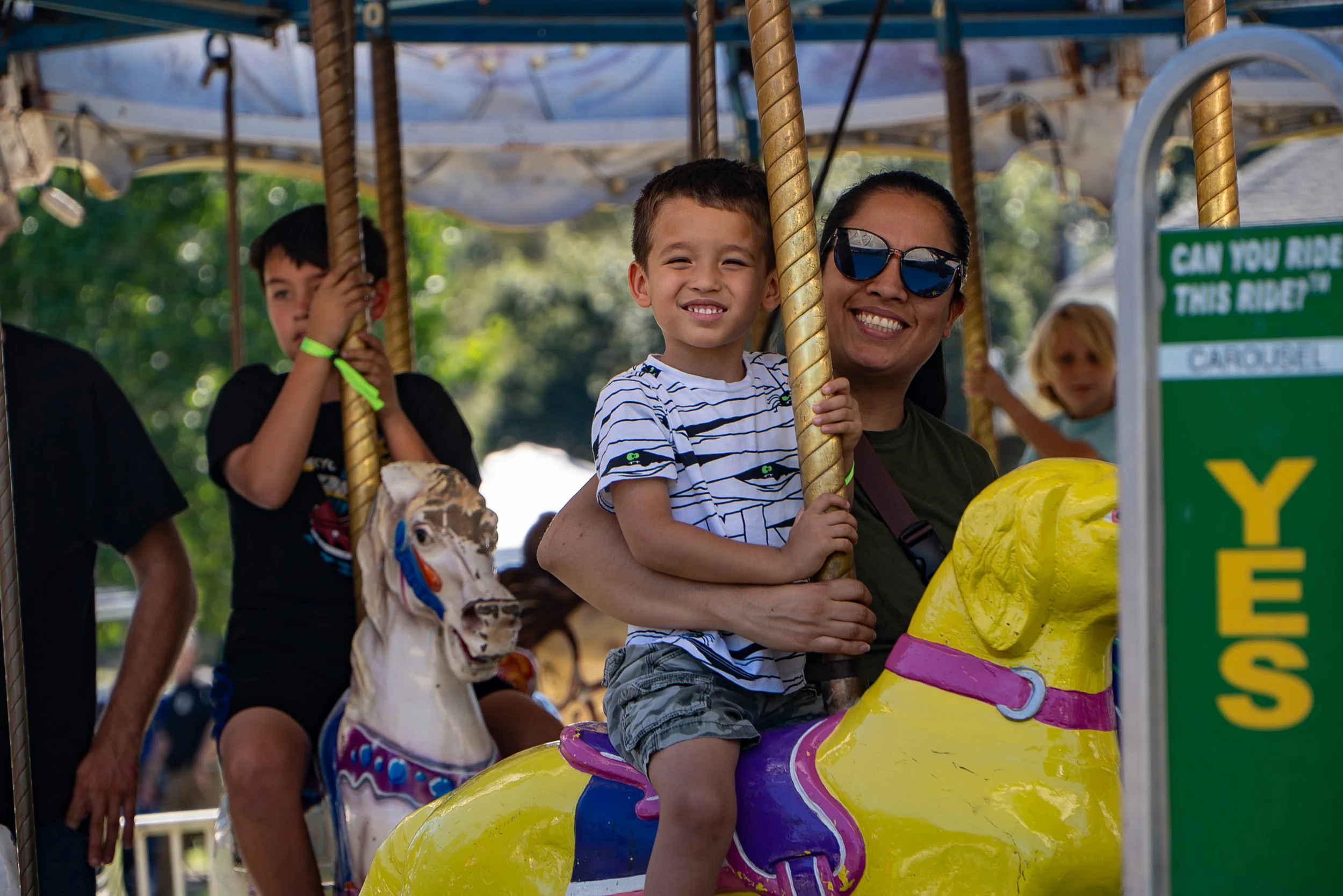 Children and an adult riding a carousel horse at an amusement park, smiling and having fun.