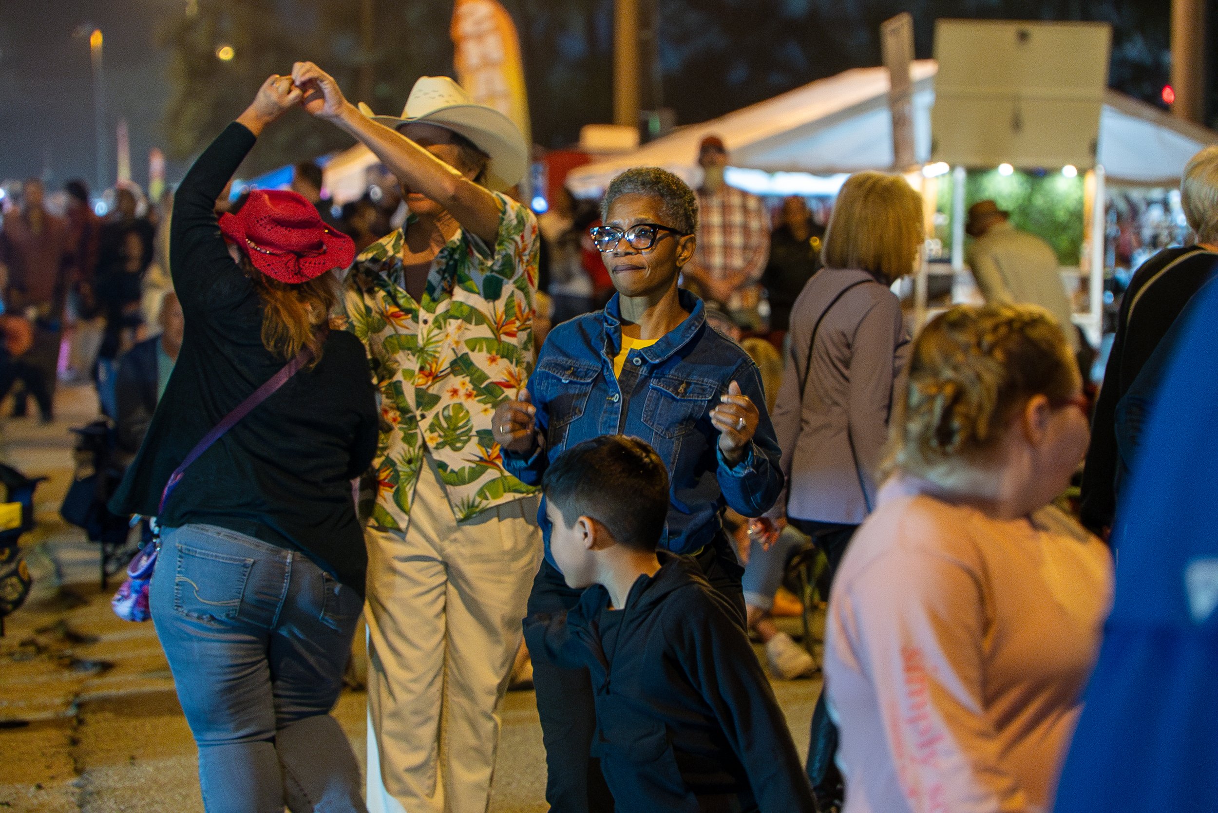 People dancing and socializing at an outdoor evening event with tents and string lights.