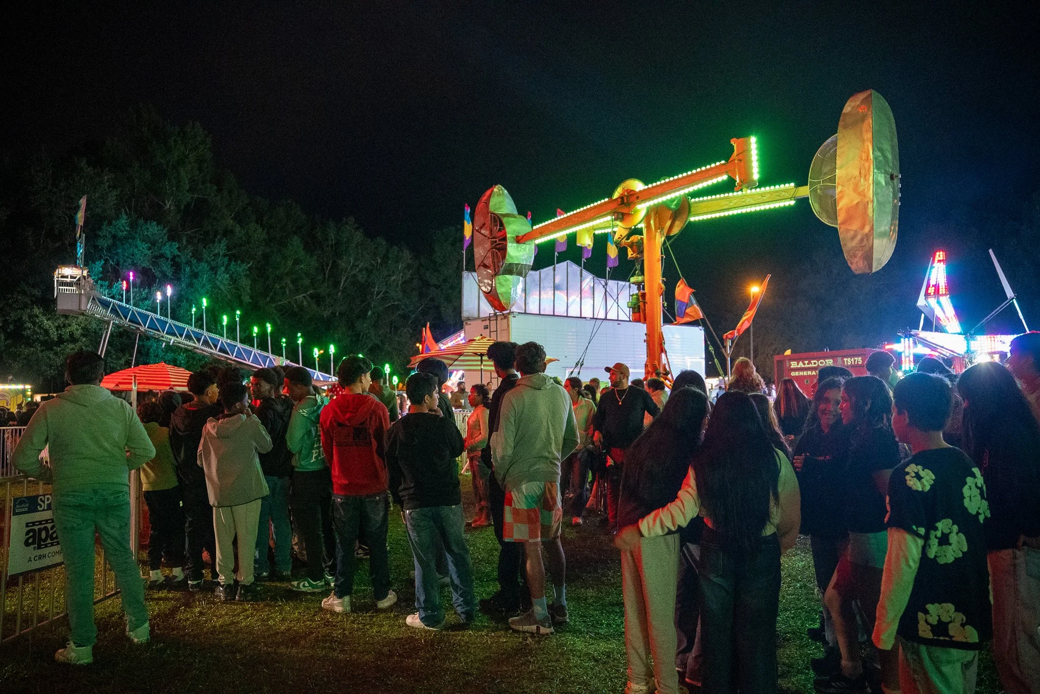 Night scene at a festival featuring a crowd of people watching rides with colorful lights.