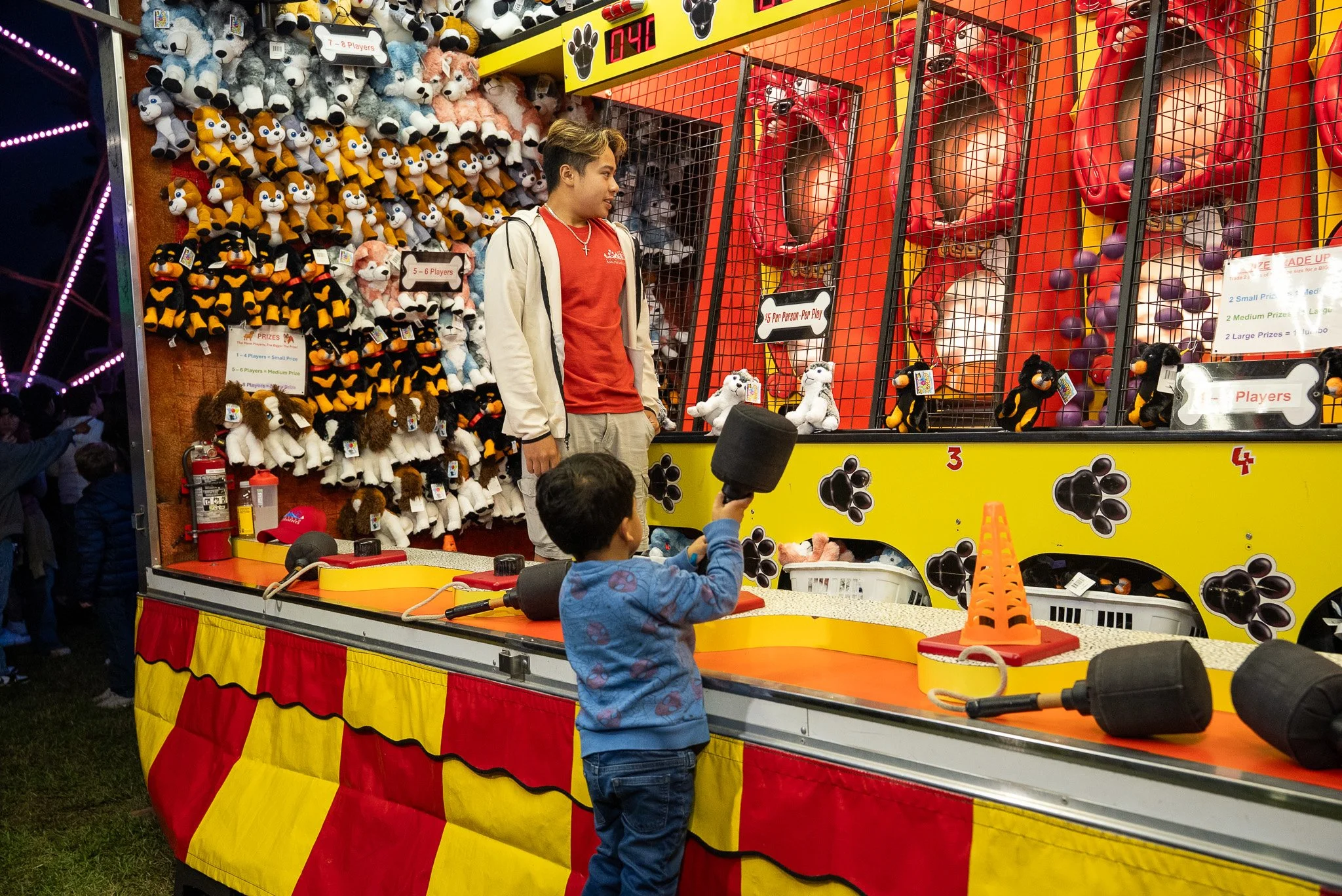 A carnival game booth with stuffed animal prizes on the left side, including various plush dogs and cartoon characters.
