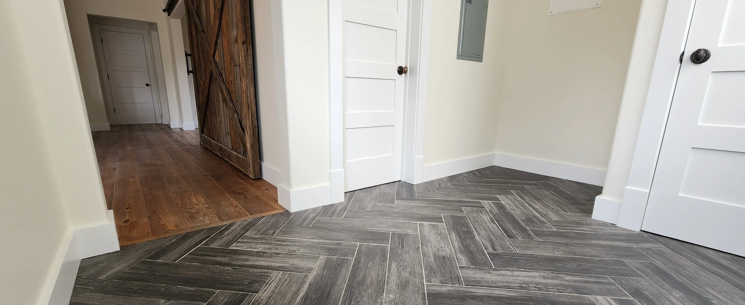 A hallway with a transition from dark wood flooring to gray tile flooring, showcasing plinth blocks and fine outside corners.
