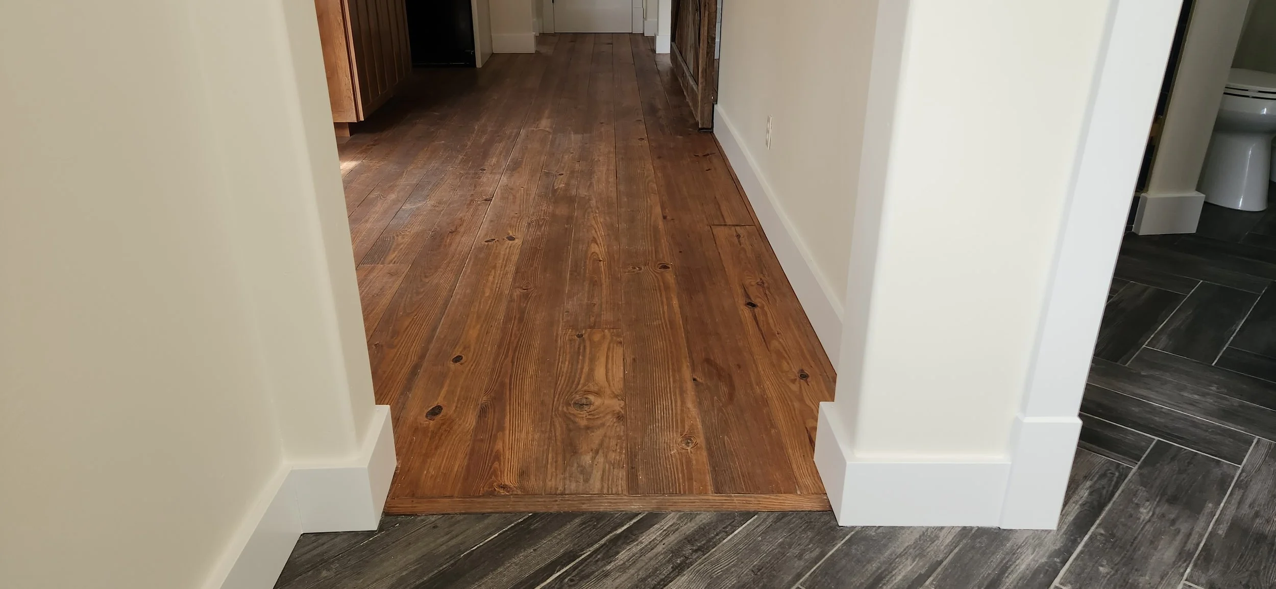 Close-up of an throughway transitioning from  dark gray tile to dark wood floors. On either side is a wrap around of immaculate base trim outside corners.