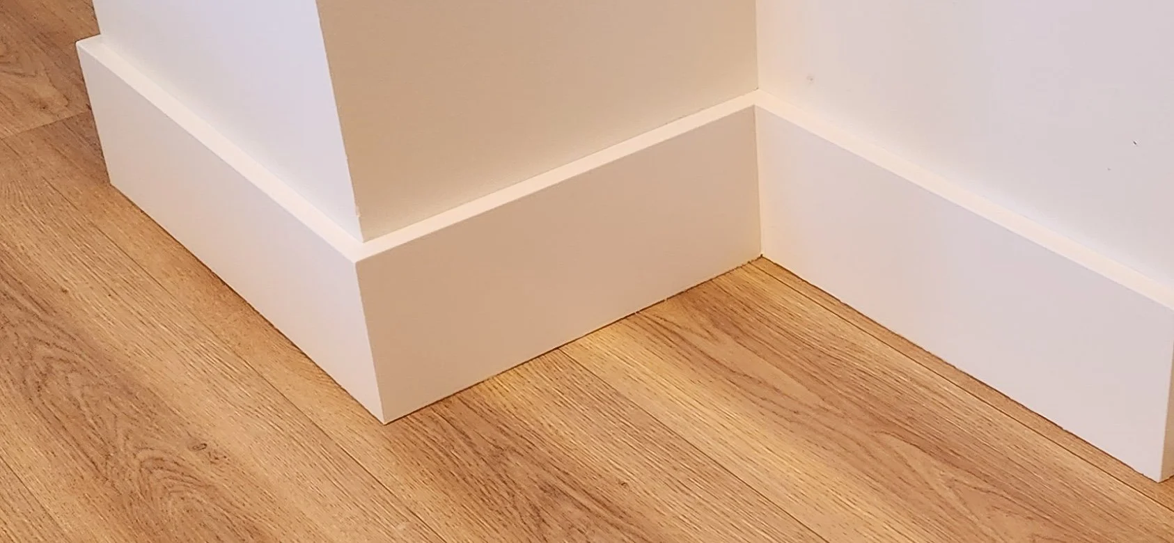 Close-up of the corner where a white baseboard meets a wooden floor in a room.