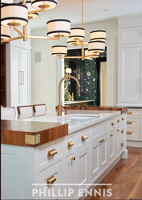 Modern kitchen island with white cabinetry, gold hardware, a marble countertop, and a brass faucet. Hanging light fixture with multiple circular lights.