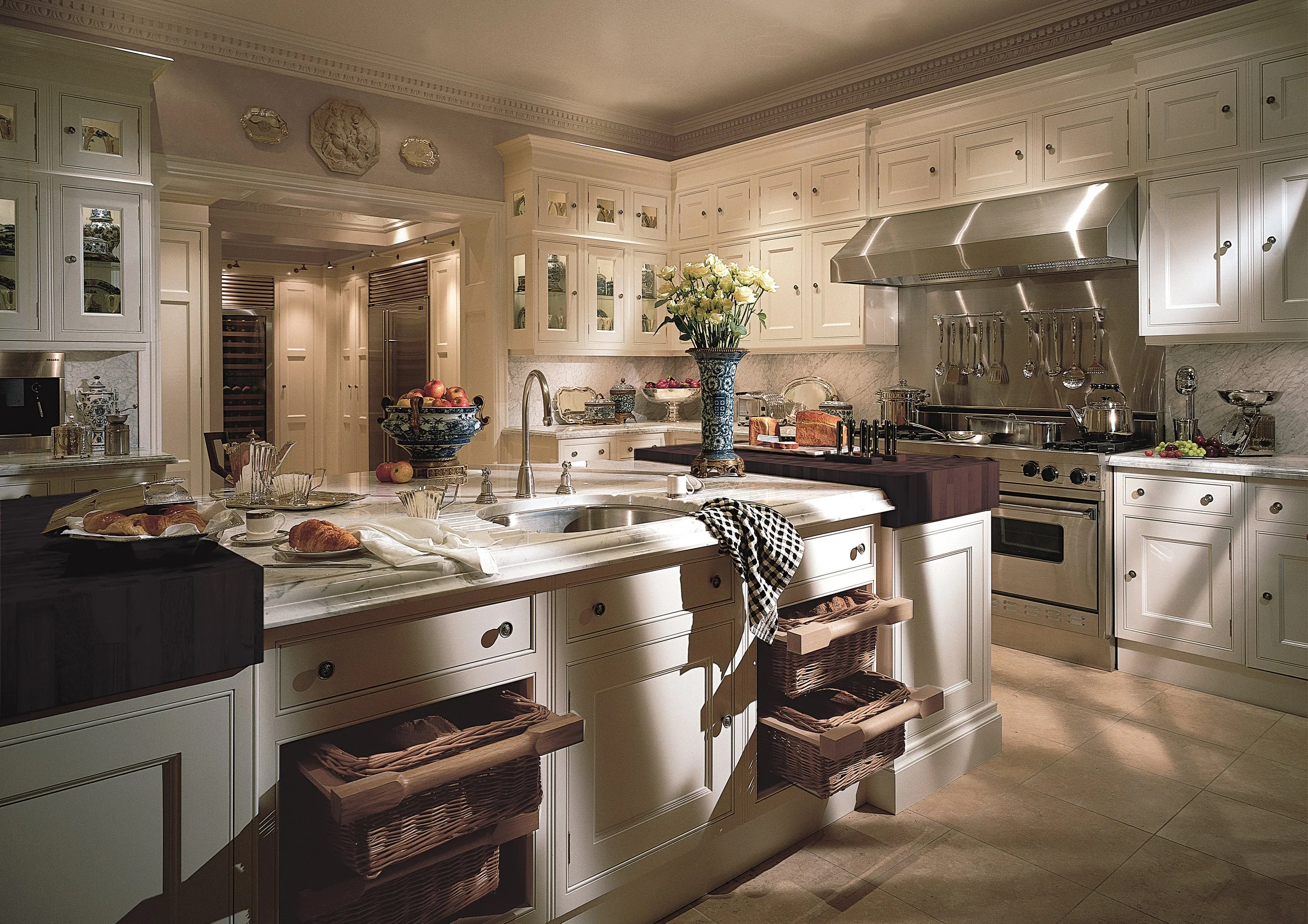 A spacious and elegant kitchen with white cabinetry, marble countertops, and stainless steel appliances, decorated with flowers and breakfast foods.