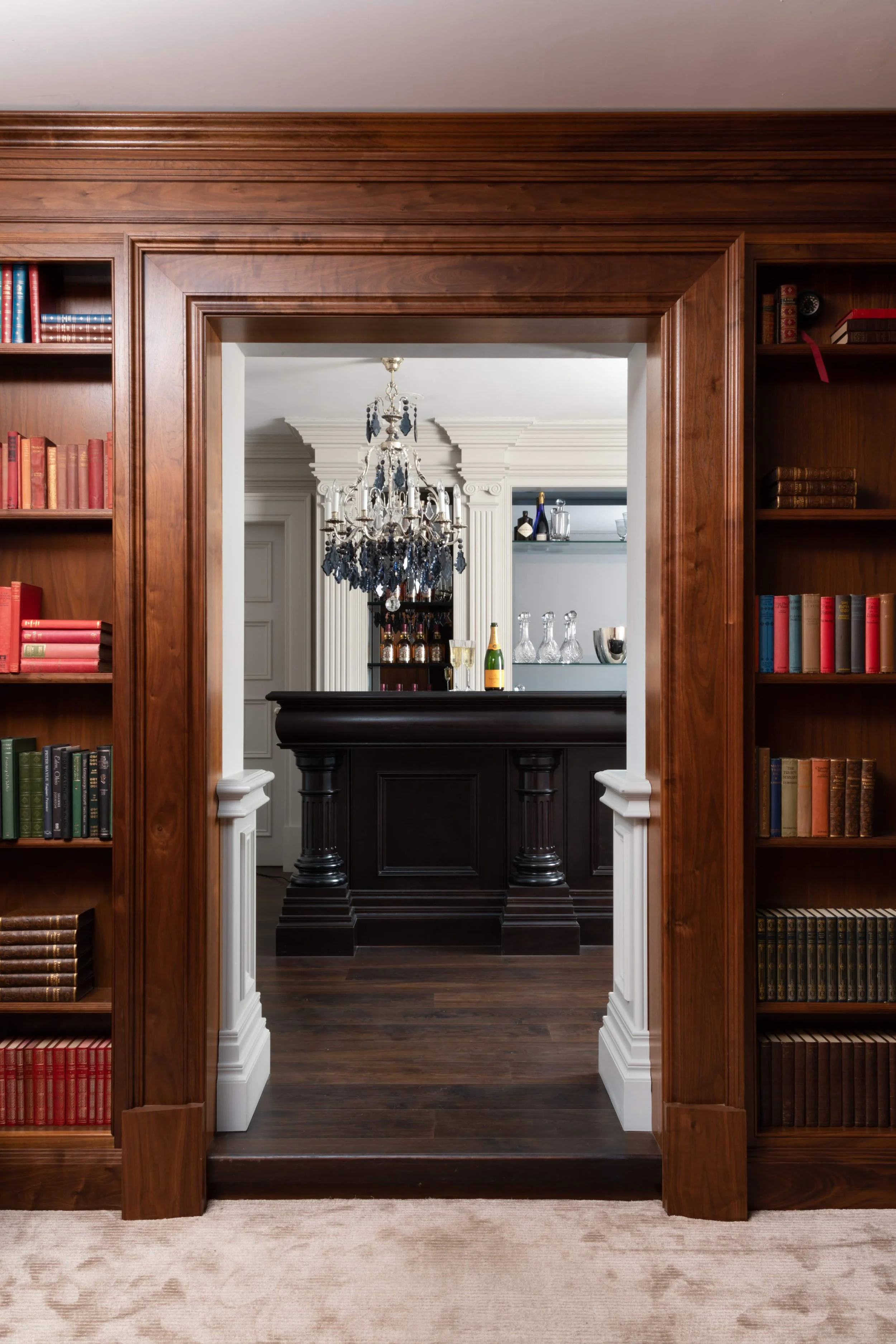 Clive Christian library with built-in bookshelves leading to a bar area.