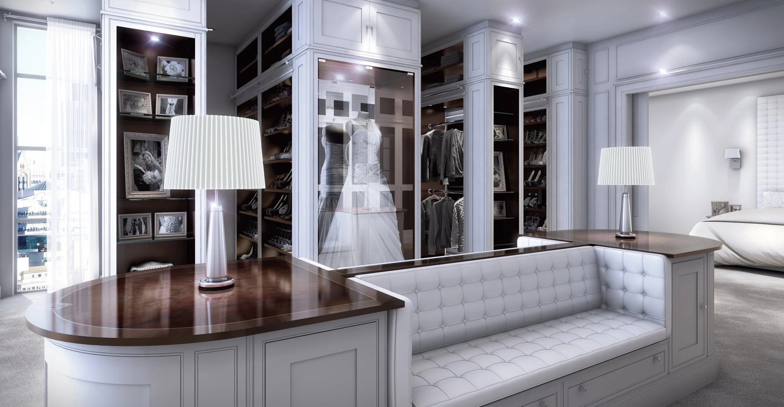 A walk-in closet with white cabinetry and shelves, featuring a glass display case with a wedding dress, surrounded by clothing, shoes, and framed photos on dark background shelves. There is a white tufted bench and two table lamps with white shades.
