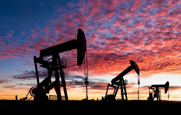 Silhouettes of oil pump jacks against a colorful sunset sky.