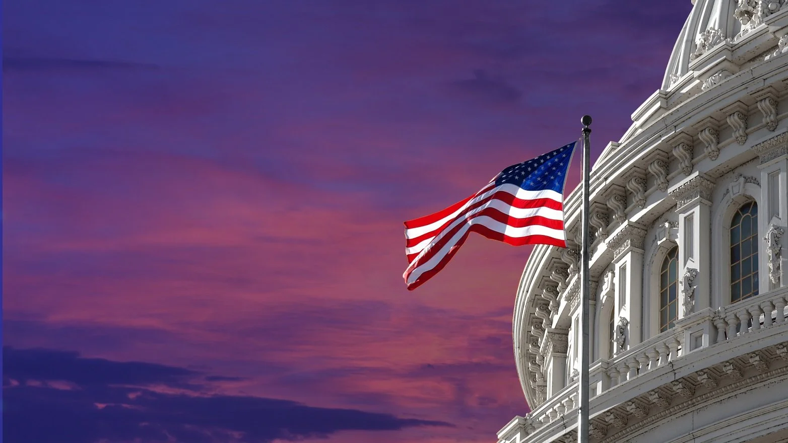 American flag flying outside the White House during sunset with a pink and purple sky.