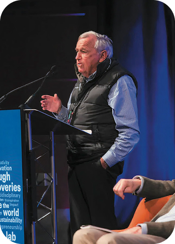 An older man speaking at a podium during a conference or event.