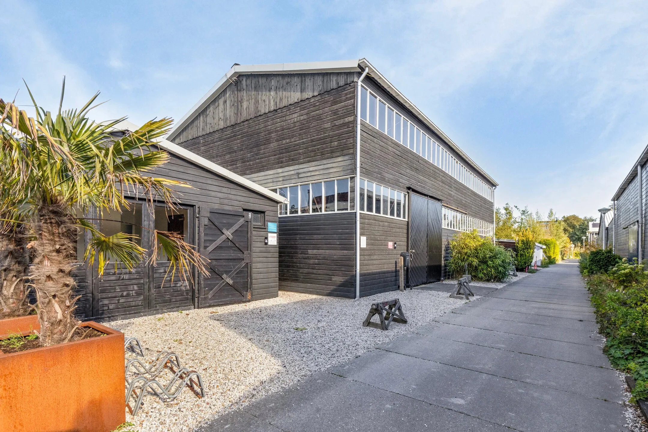 Moderne zwarte houten gebouwen langs een voetpad, met planten en blauwe lucht.