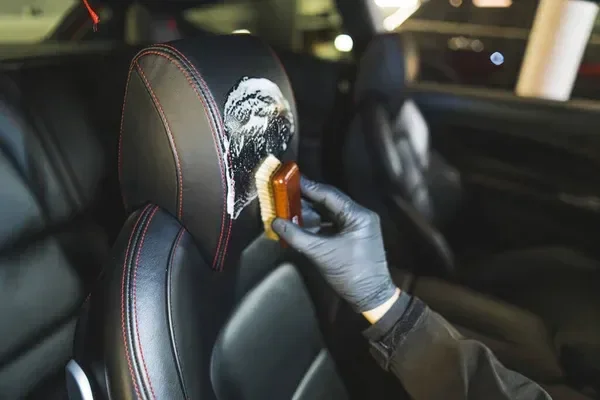 Gloved technician cleaning a leather car seat with a detailing brush