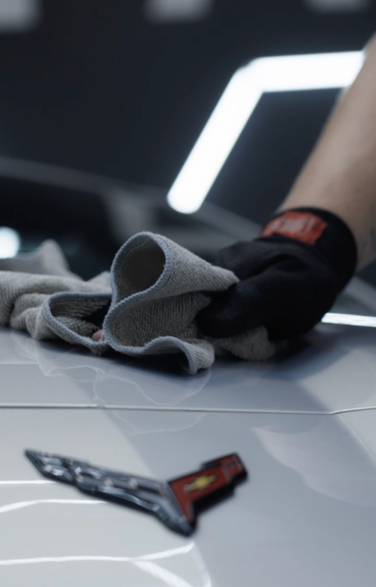 Technician machine polishing the hood of a silver Corvette