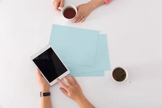 Person holding a smartphone with two cups of coffee on a white table.