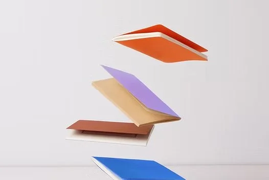 A stack of four colorful notebooks with different colors and sizes, floating against a plain background.