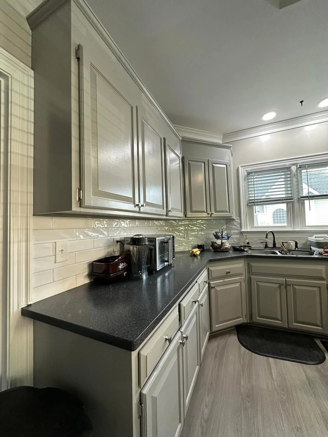 Kitchen with gray cabinets and black countertop, white tiled backsplash, window over sink, and small appliances on counter.